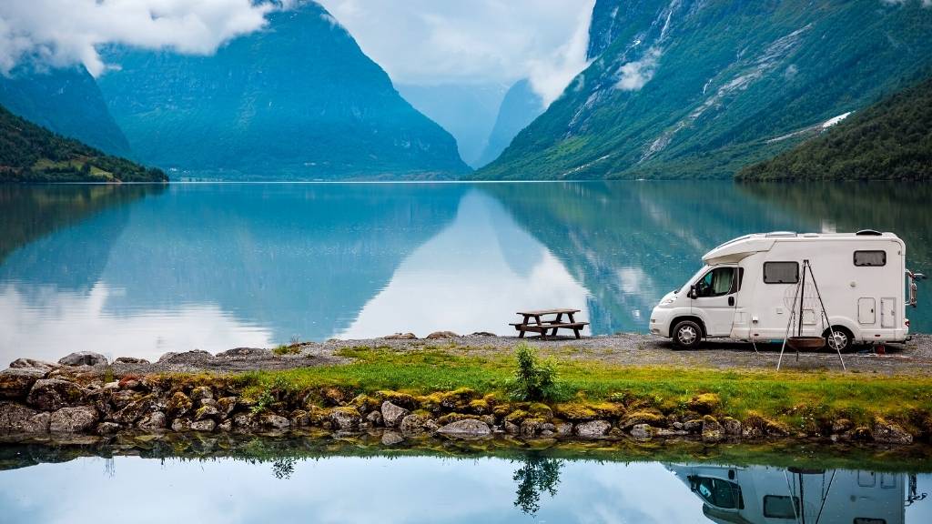 Campervan parked on a lake overlooked by mountains